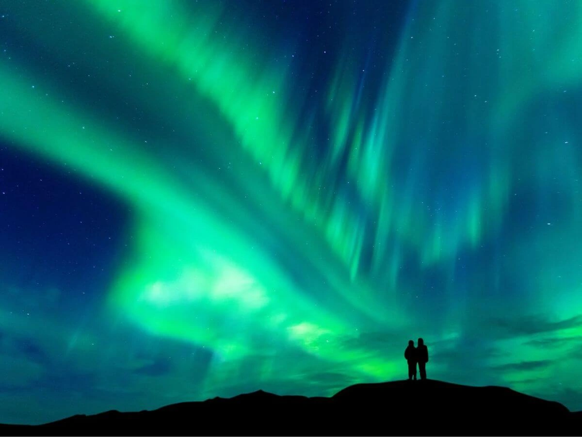 Dos personas admiran las auroras boreales que iluminan el cielo nocturno de Islandia.