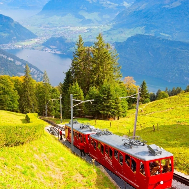 Un tren rojo avanza por una vía montañosa, rodeado de paisajes naturales impresionantes.