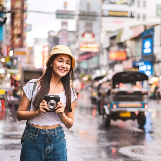 Mujer asiática capturando una fotografía en un entorno urbano, mostrando su creatividad en medio del paisaje urbano.