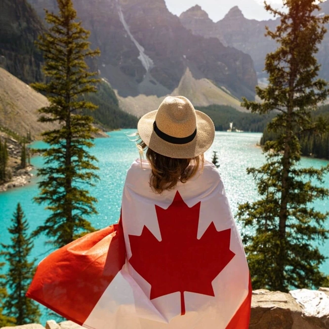 Una mujer sostiene con orgullo una bandera canadiense en la cima de una montaña, rodeada de un impresionante paisaje natural.