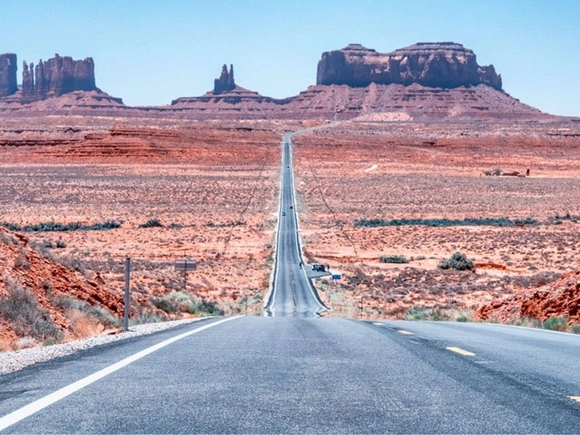 Camino que conduce a Monument Valley, rodeado de formaciones rocosas icónicas y un vasto paisaje desértico.