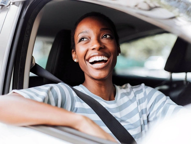 Una mujer sonriente se sienta en el asiento del conductor de un coche, rebosando confianza y alegría mientras se prepara para conducir.