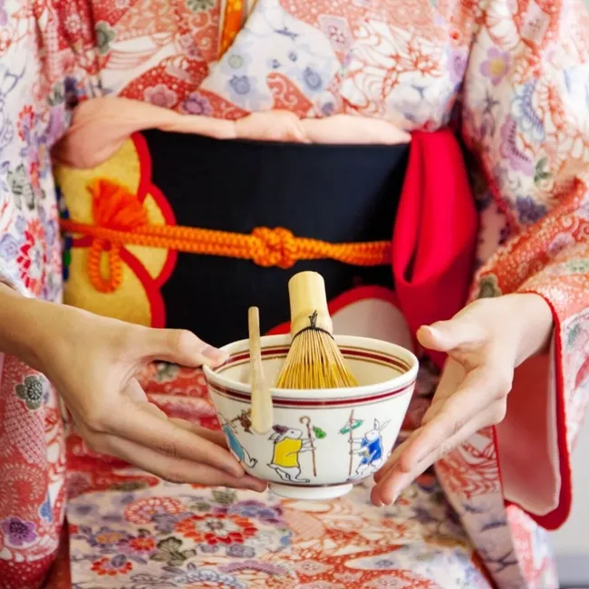 Una mujer vestida con un kimono tradicional sostiene con gracia un cuenco de té, encarnando la elegancia y el patrimonio cultural.