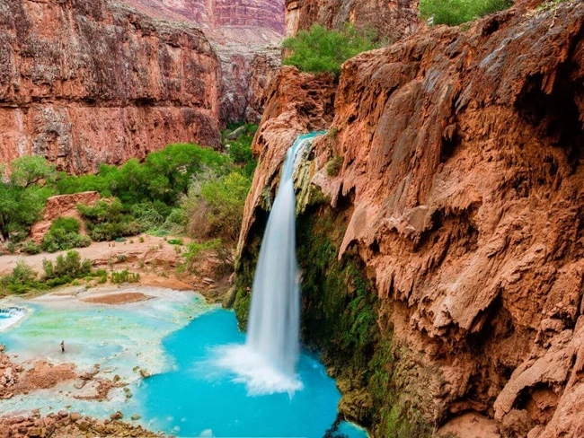 Una vívida cascada que cae en un estanque turquesa rodeado de rojos acantilados rocosos y verde follaje.