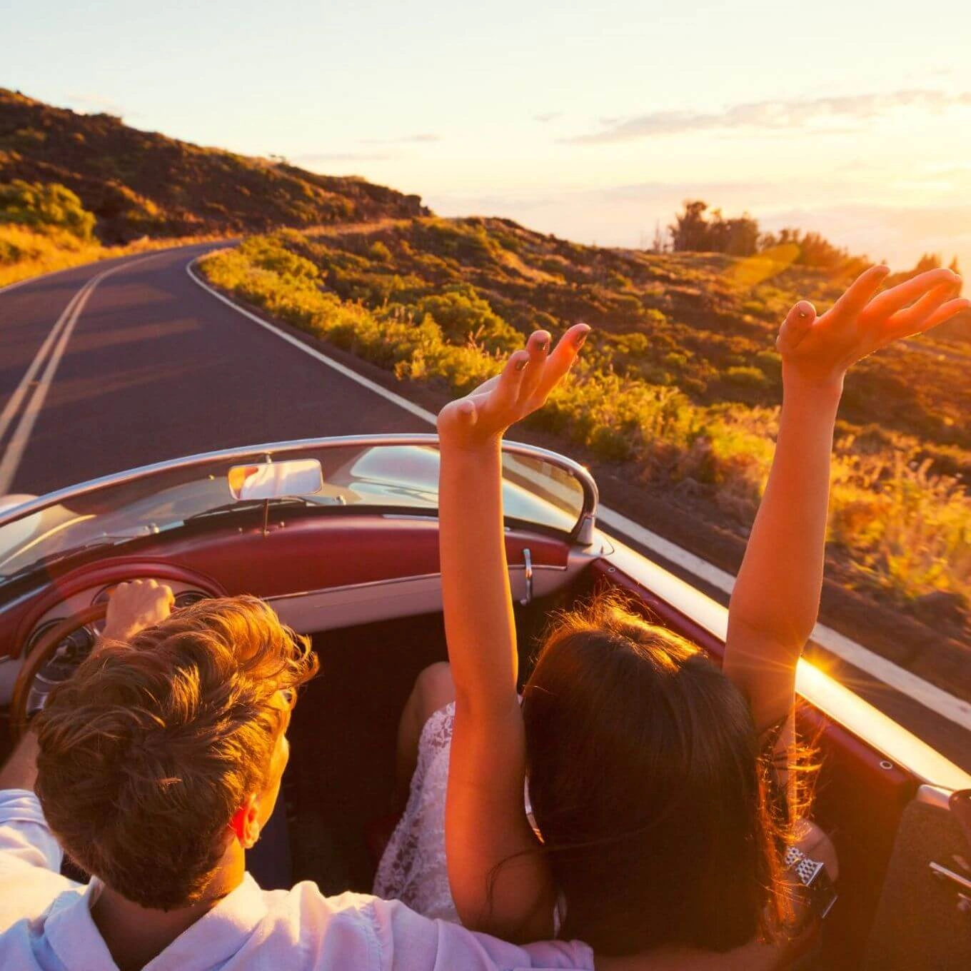 Una pareja disfruta de un paseo panorámico en un coche descapotable, disfrutando del cálido resplandor de una puesta de sol.