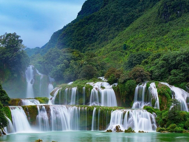 Una vista serena de cascadas que caen en cascada a través de un vibrante y exuberante bosque verde, rodeado de rico follaje y belleza natural.