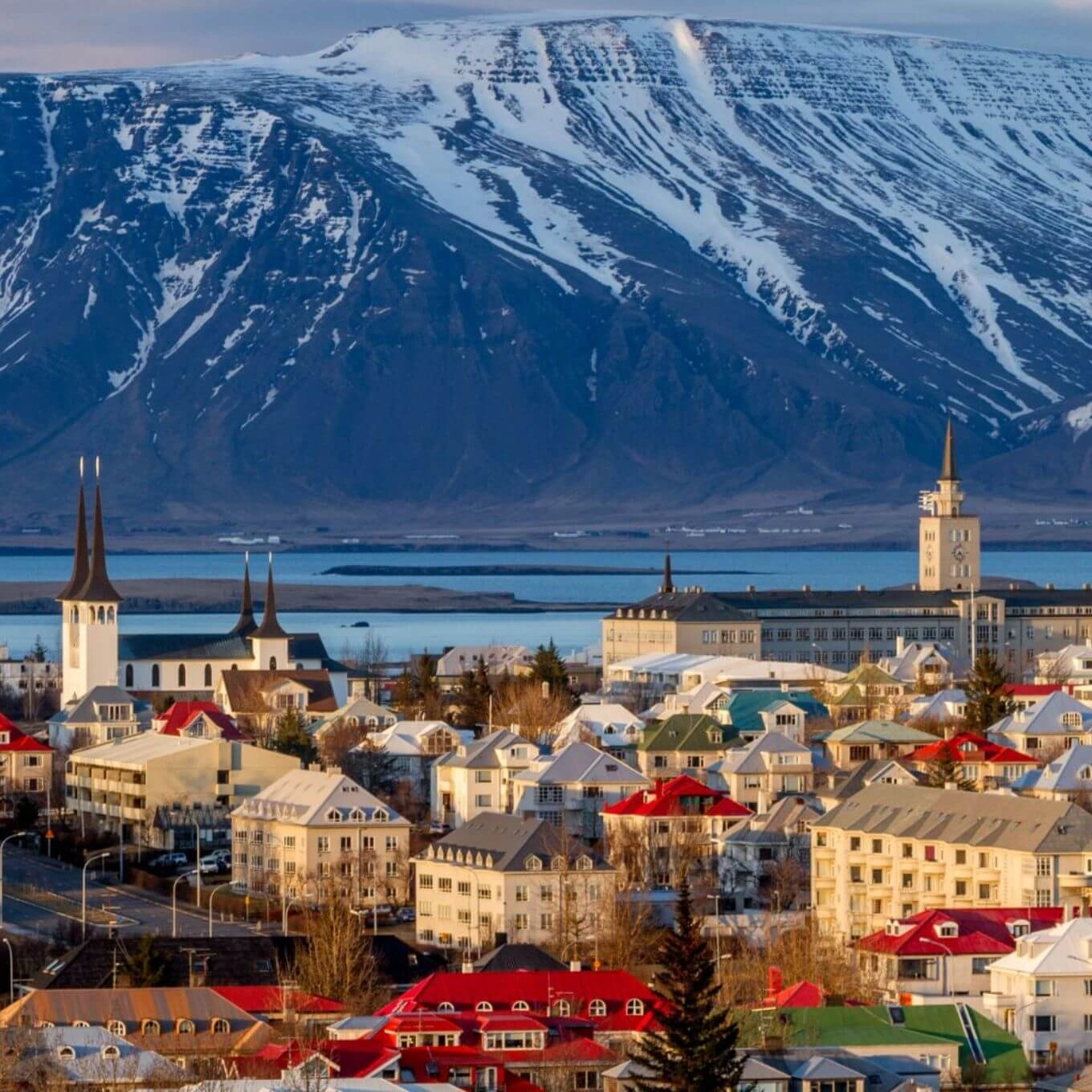 Vista panorámica de Reikiavik, Islandia, con edificios de colores sobre un fondo de montañas y un cielo azul despejado.