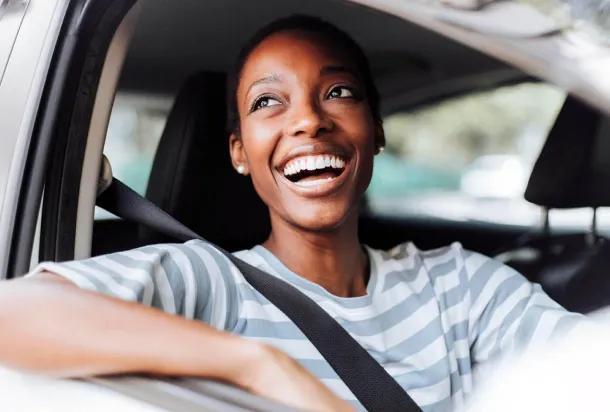 Una mujer sonriente se sienta en el asiento del conductor de un coche, rebosando confianza y alegría mientras se prepara para conducir.