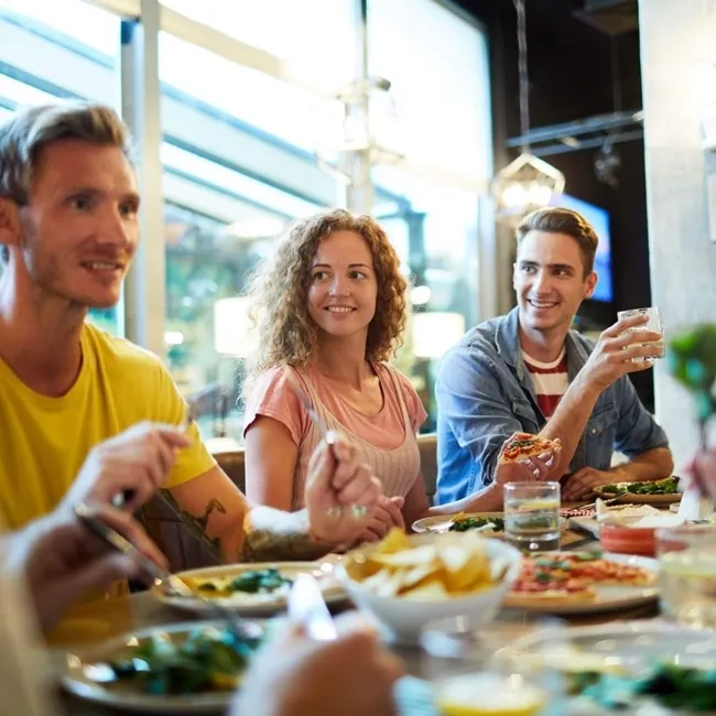 Un grupo heterogéneo de personas reunidas en torno a una mesa, disfrutando de una comida en un ambiente cálido y acogedor.